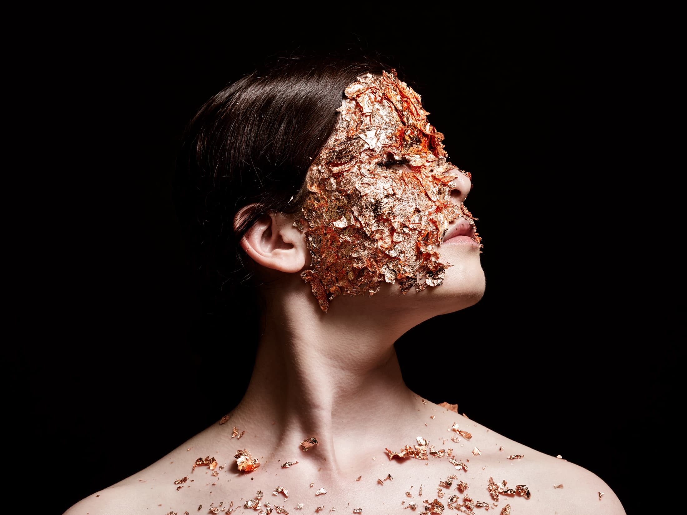 Maya Fridman, her face covered in gold leaf, against black