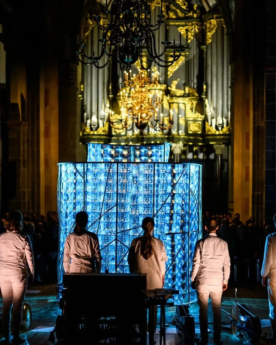 An installation of light in a church, performers in white standing before it