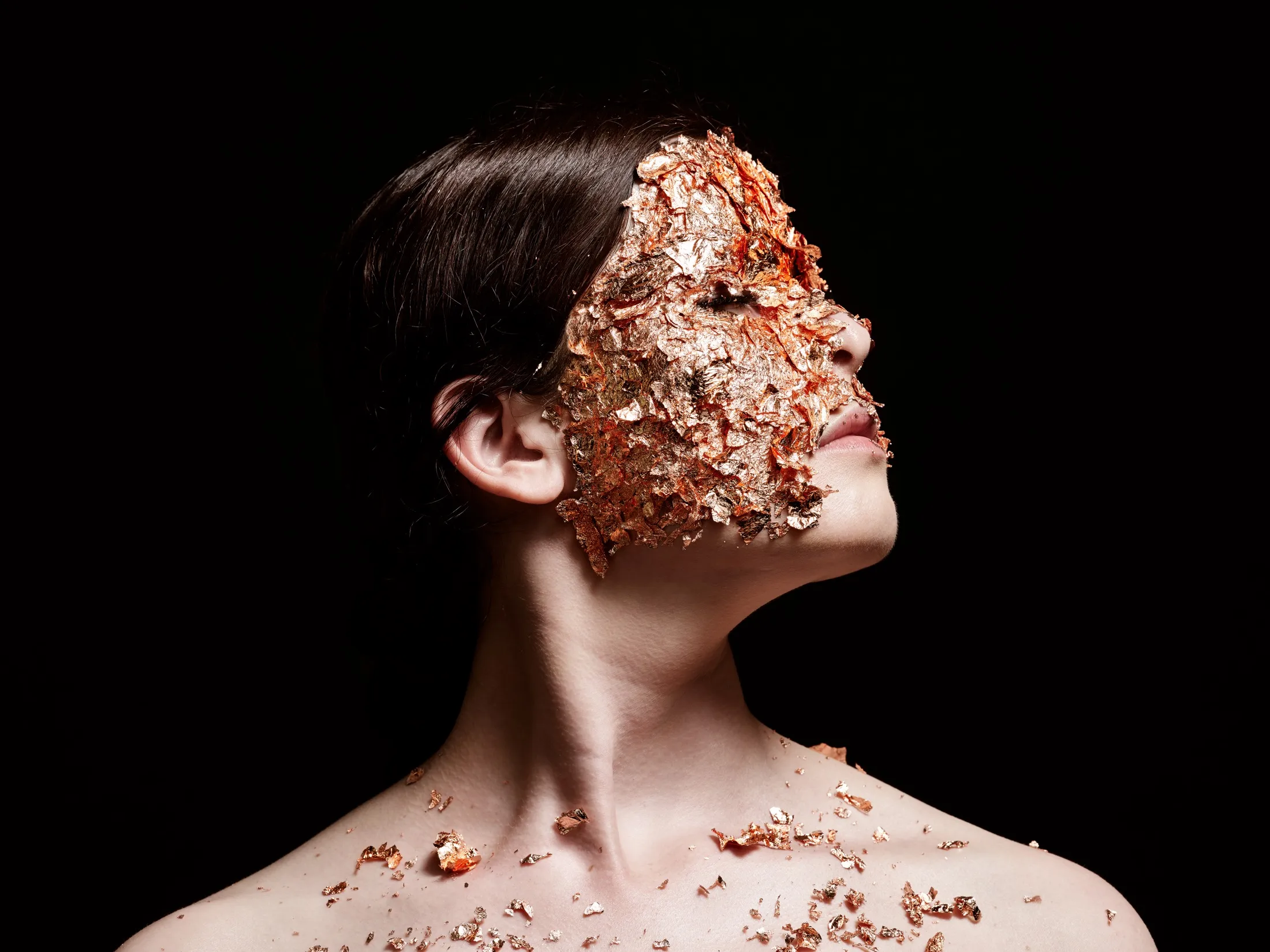 Maya Fridman, her face covered in gold leaf, against black